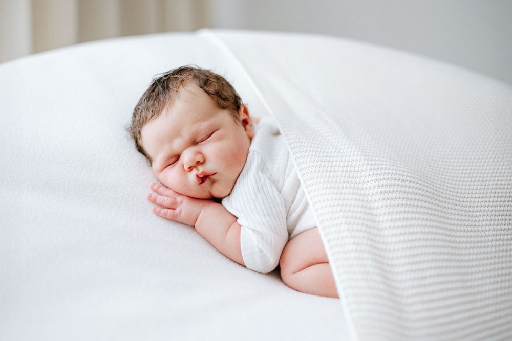 Sleeping newborn baby wrapped in white blanket lying on soft white bedding.