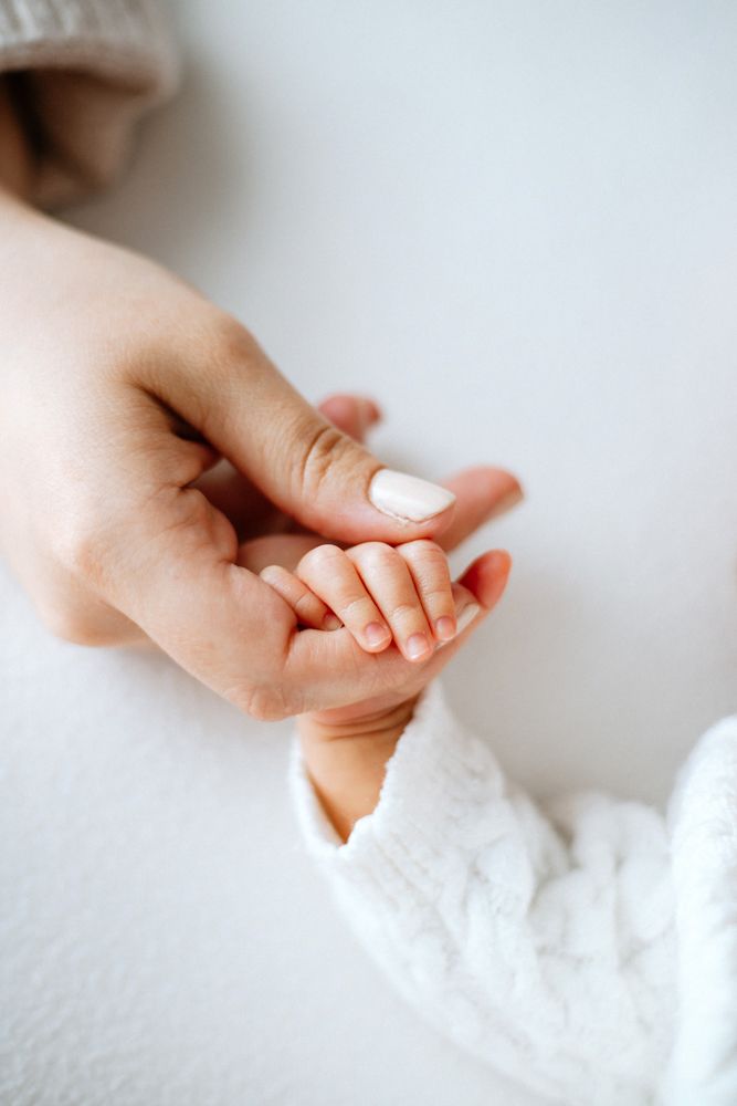 A tender moment of an adult hand gently holding a small baby's hand against a soft white background.