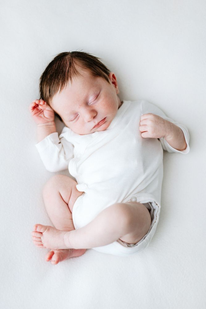 Sleeping newborn baby wearing white onesie lies peacefully on light background.