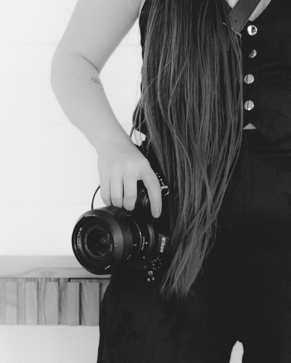 Black and white portrait of a woman with long hair holding a Nikon camera at her side.