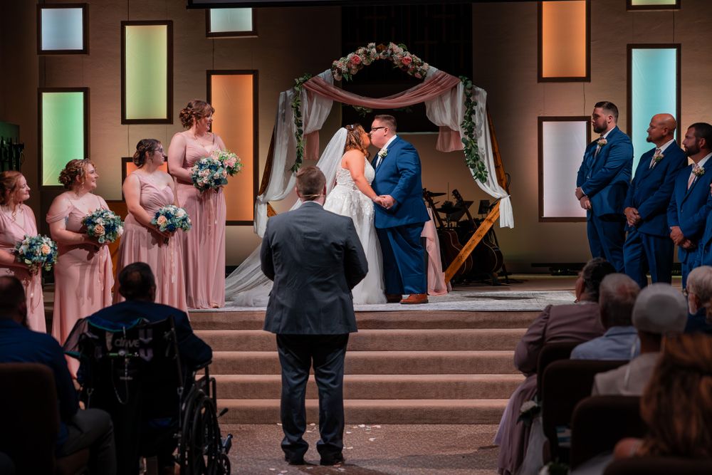 Wedding ceremony taking place on stairs under an ornate arch with bridesmaids in pink dresses and guests seated in the audience.