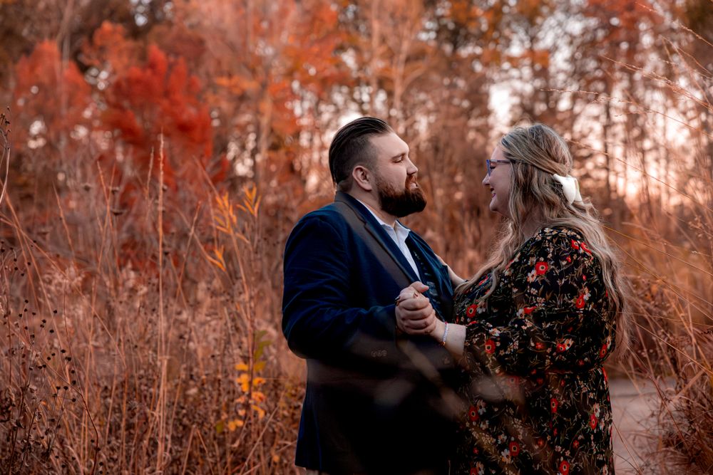 A couple shares a romantic moment together in tall autumn grass during sunset, wearing navy and floral outfits.
