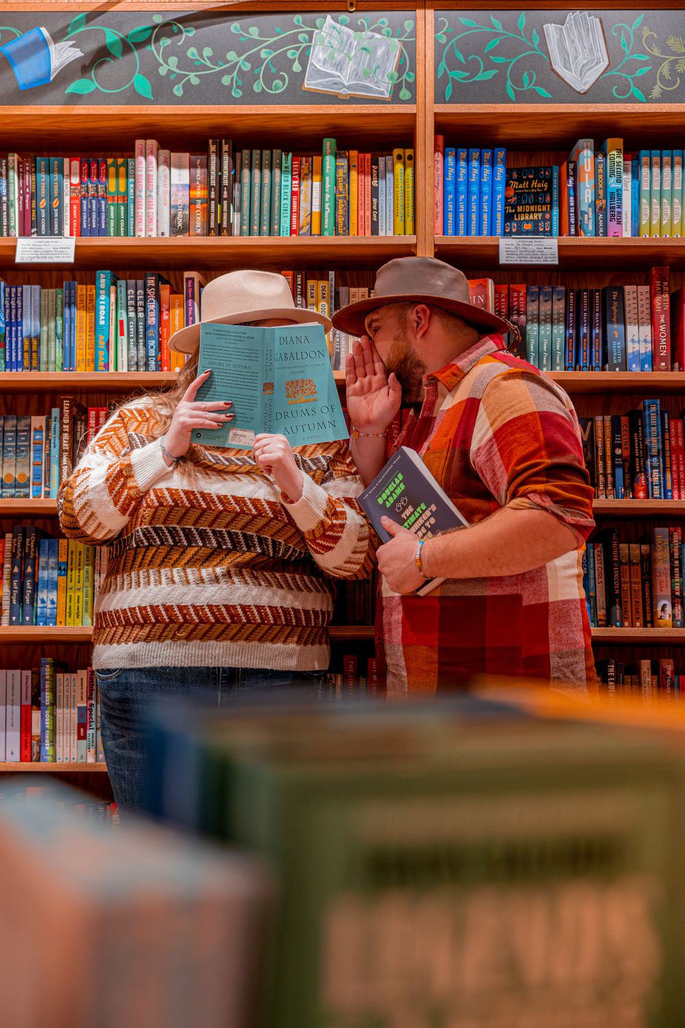 Two people browse books together in a cozy bookstore with colorful bookshelves in the background.