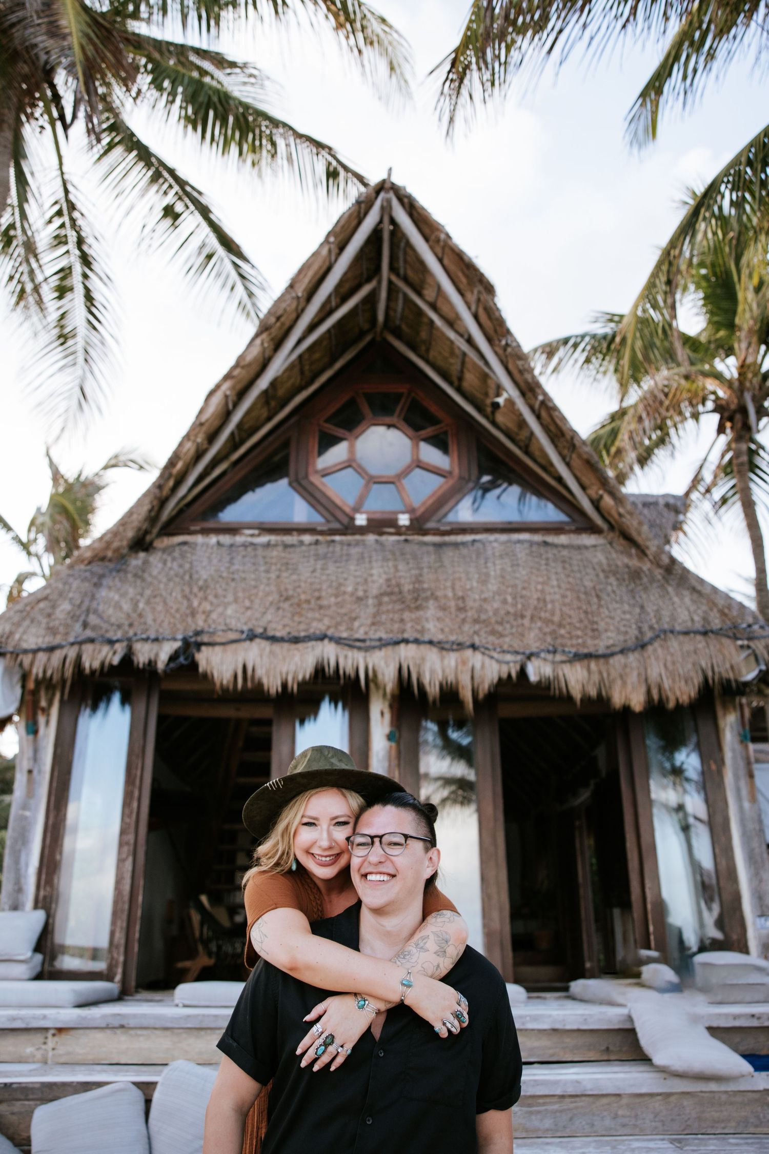A couple hugging during their engagement session with a cabana in the background among the palm trees of Tulum