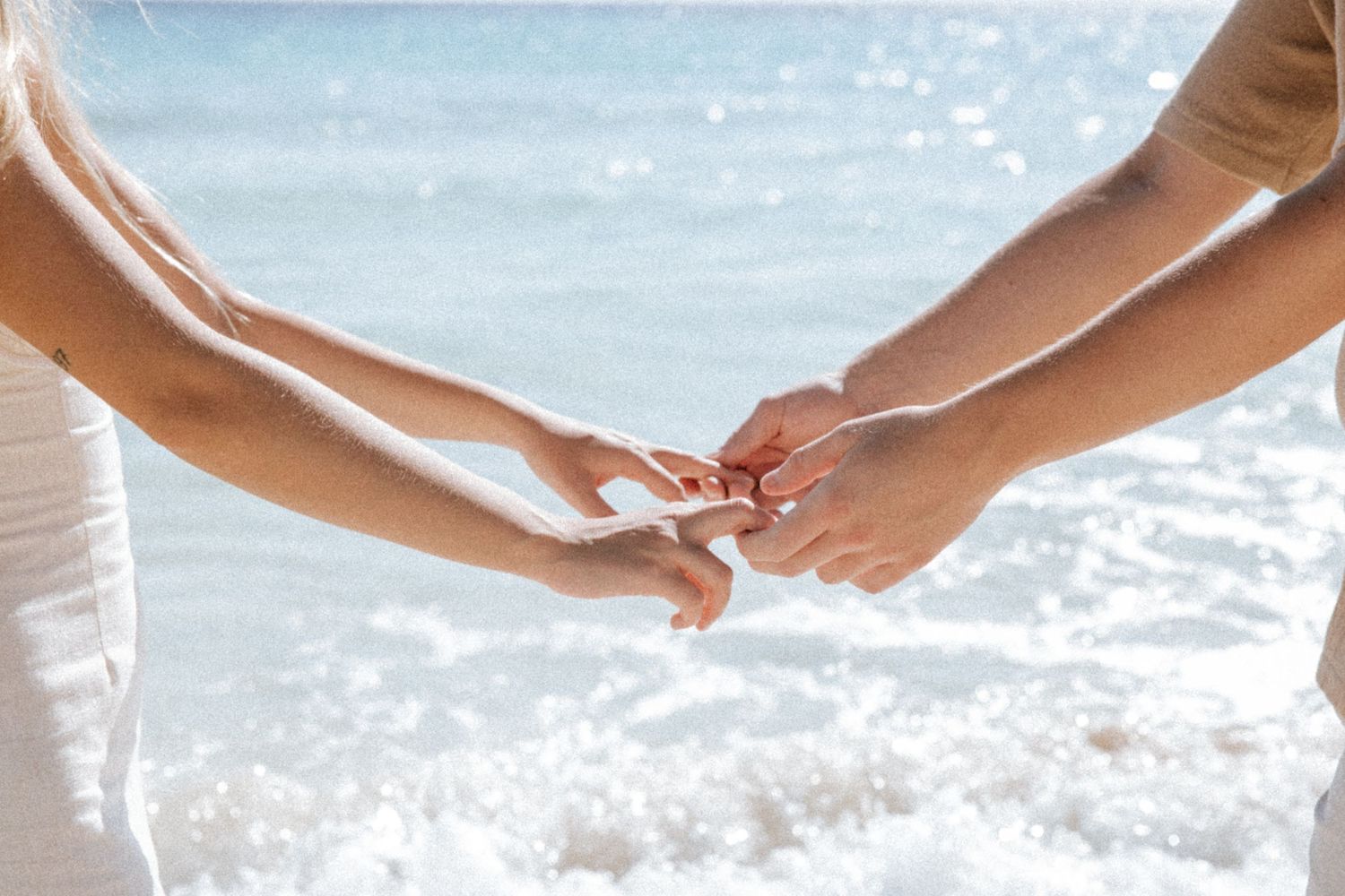 Couple holding hands with the white foam of the sea in the background, bathed in bright, soft light on a morning in Tulum