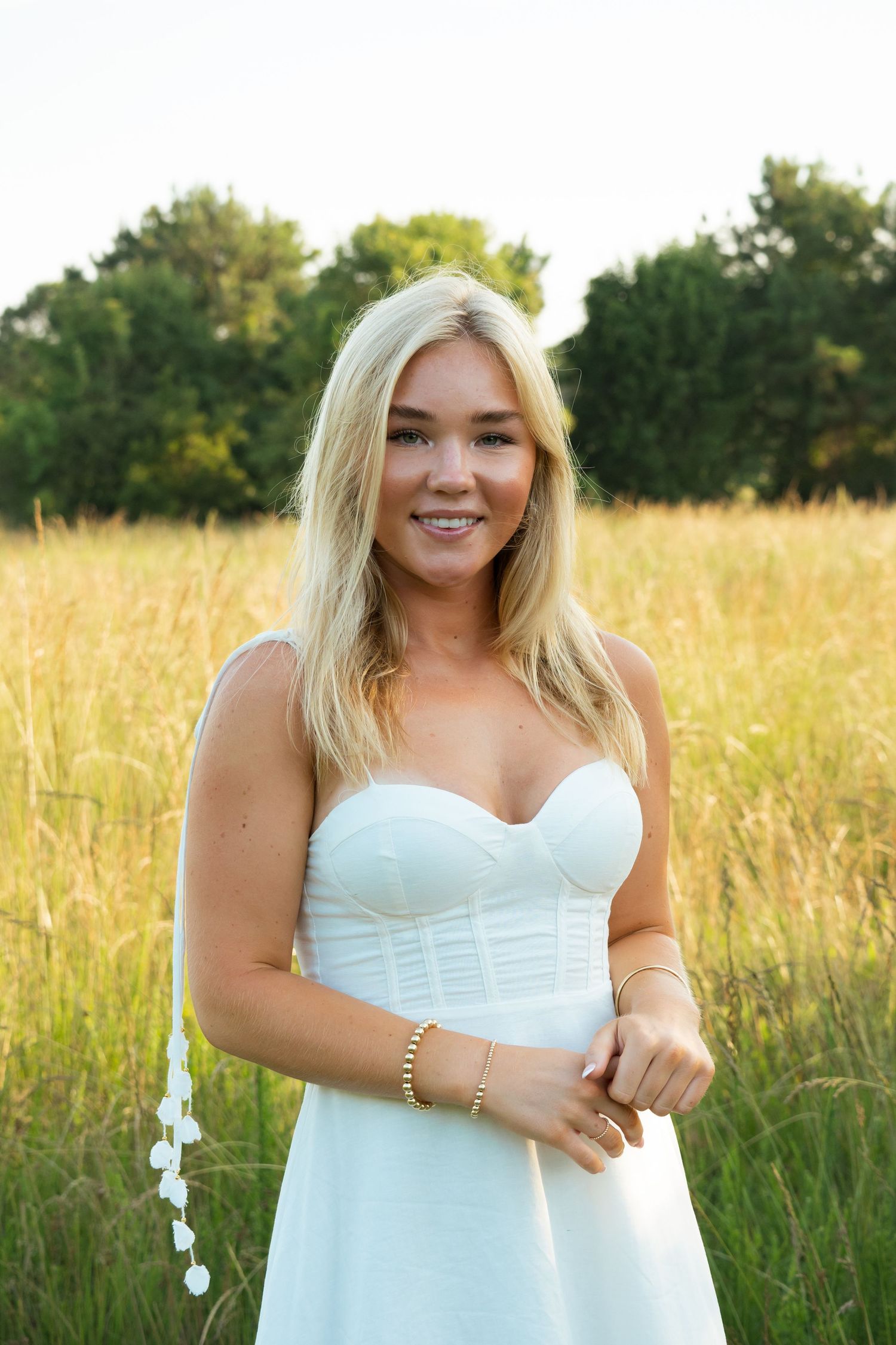 Summer portrait of someone in a white dress standing in a golden wheat field.