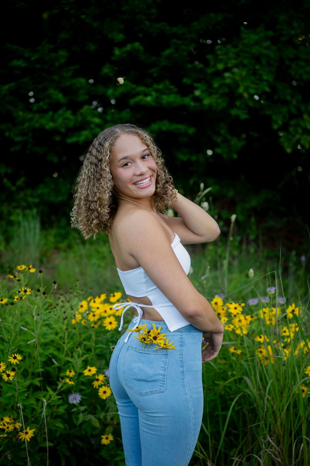 A person in jeans and white top poses in a wildflower field with yellow blooms.