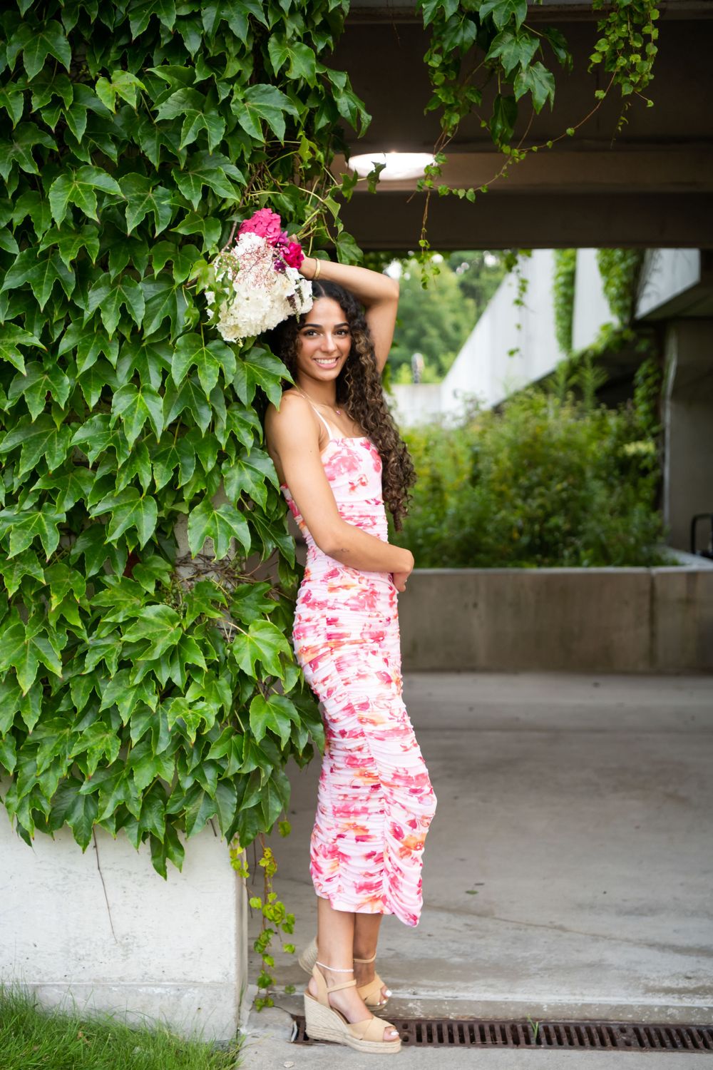A summer portrait pose against ivy-covered walls wearing a pink floral dress.