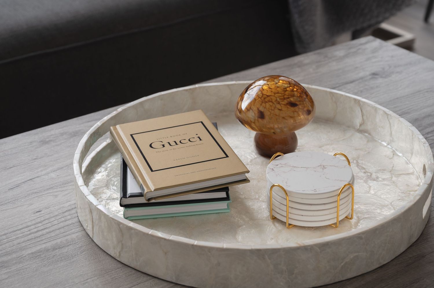 A marble tray displays Gucci books, a decorative golden round box, and a brown circular object on a light surface.