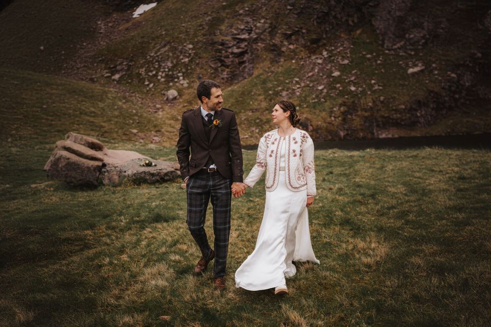 A couple walks together on rugged mountain terrain during their wedding photoshoot.