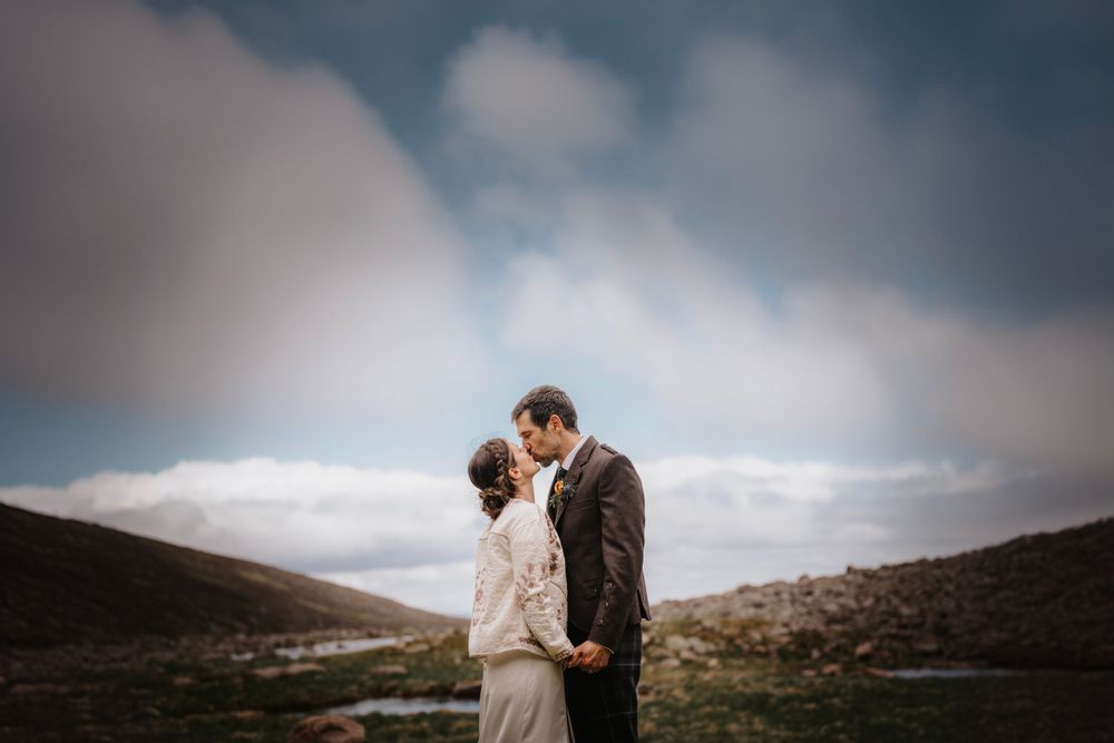 Intimate wedding portrait against moody mountain landscape and cloudy sky.