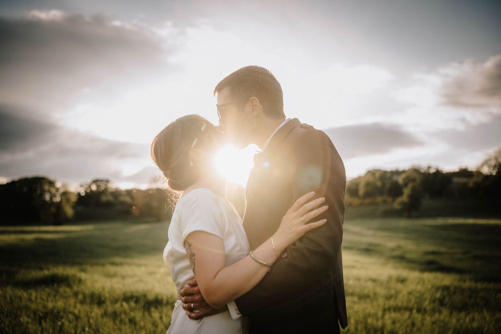 A romantic sunset silhouette of a couple embracing in a grassy field.