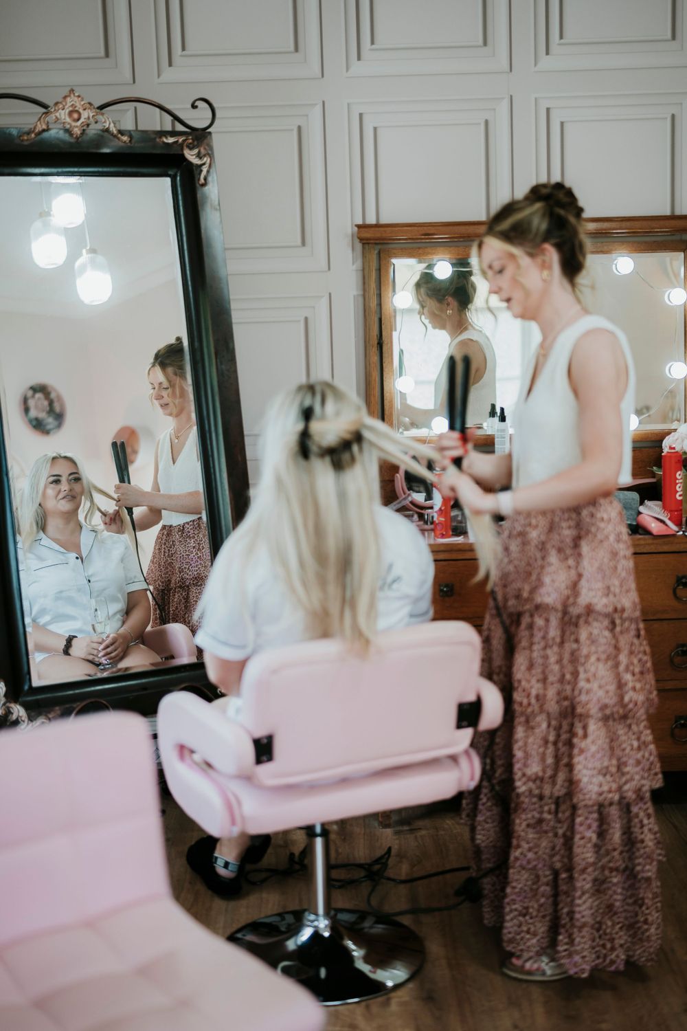 Wedding preparation scene with pink salon chair and large mirror reflecting stylist at work.