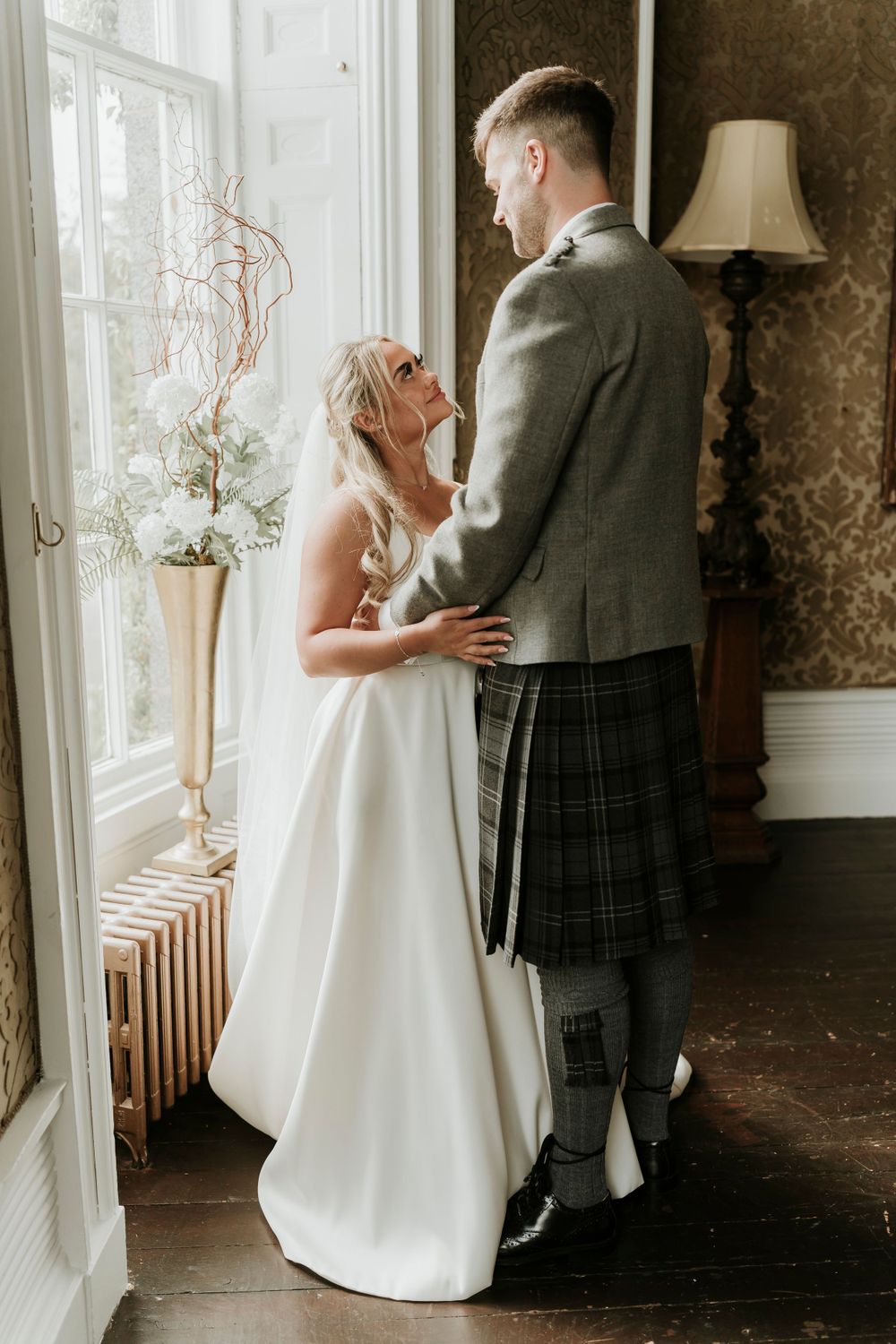 A sweet wedding moment captured by a window with natural light streaming in and elegant decor.