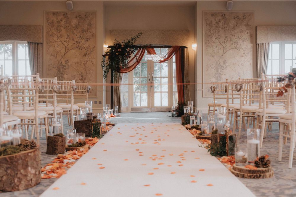 Elegant wedding ceremony setup with white aisle runner, floral arch and scattered rose petals.