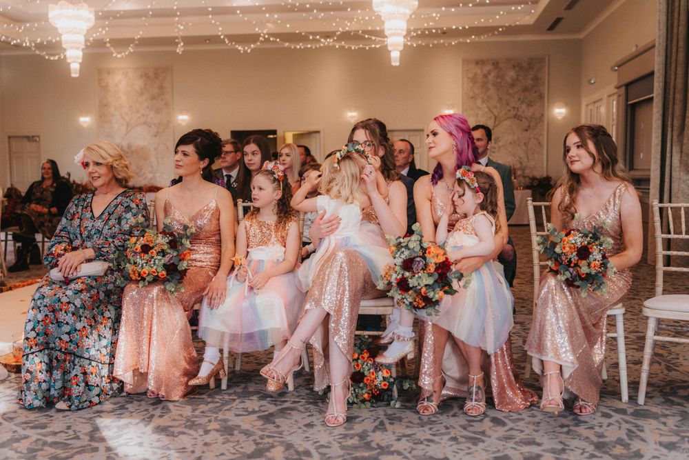Wedding party members seated in pink dresses share laughs during a candid reception moment.
