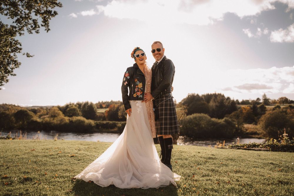 Scottish wedding couple posing in field with groom wearing traditional kilt.