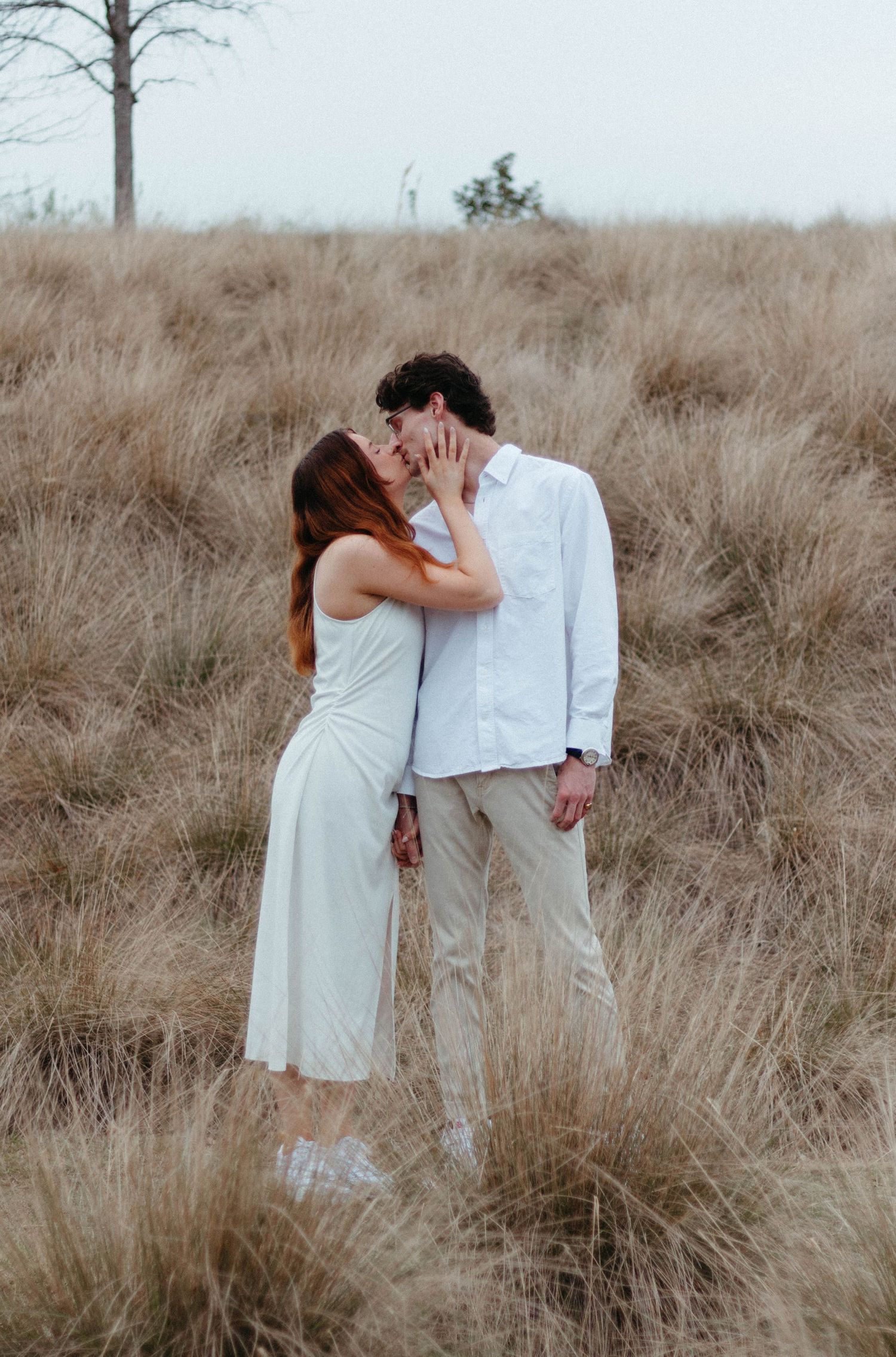 Romantic couple in white clothing sharing an intimate moment in a field of tall grass.