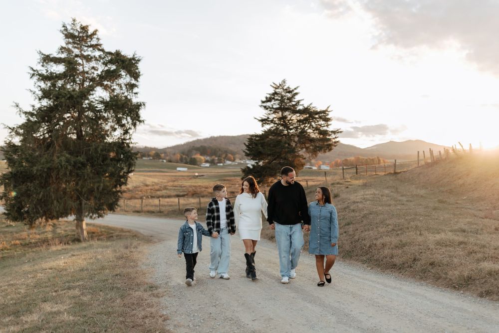 Family walks together along dirt path with sunset and mountains in background.