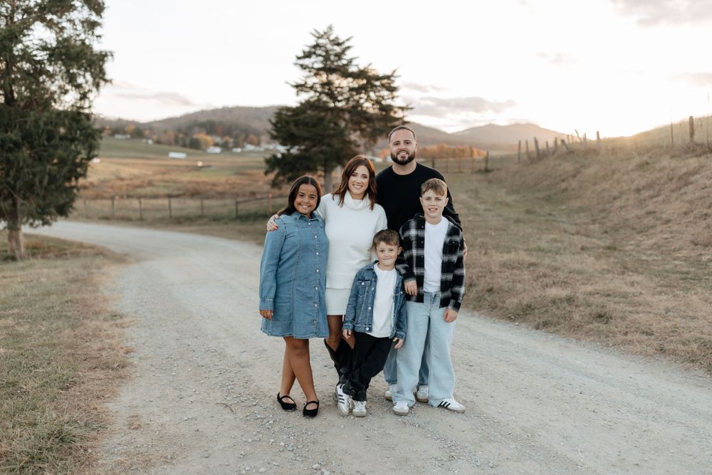 Family dressed in casual denim and white poses together on country road.