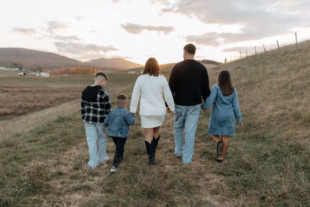 Family walking away on dirt path with rolling hills and sunset in background.