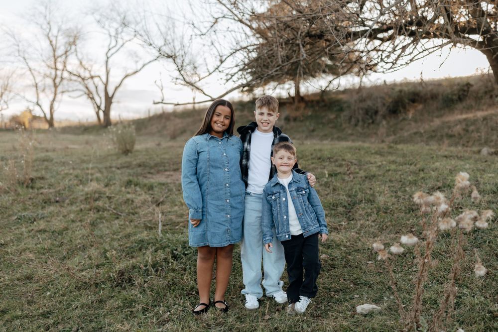 Small family group posing together on hillside during outdoor portrait session.