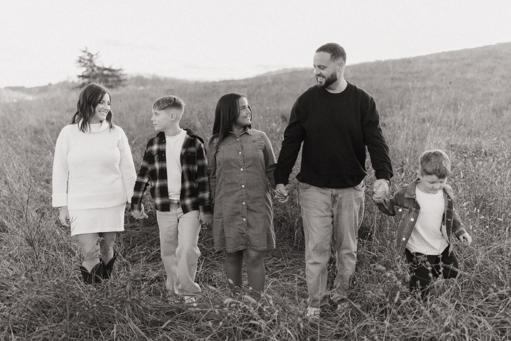 Black and white portrait of family standing together in grassy field.