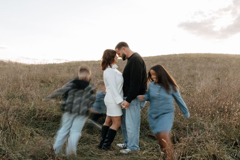 Family shares playful moment together in field during golden hour photoshoot.