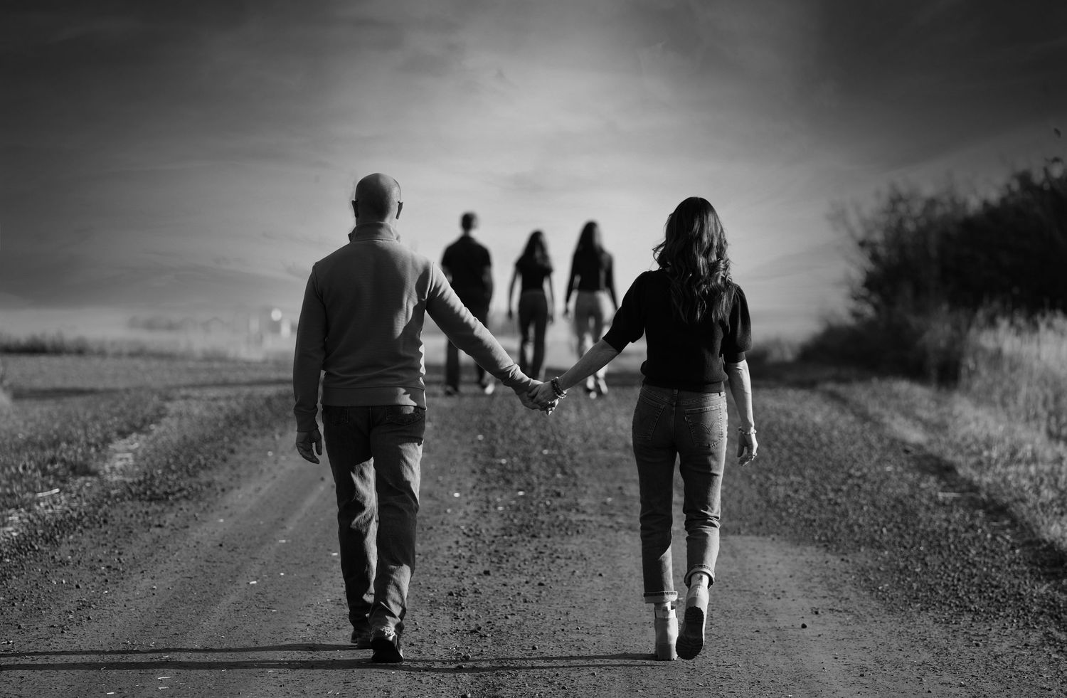 Silhouette of people walking on a dirt road with silhouettes in distance against a dramatic sky.