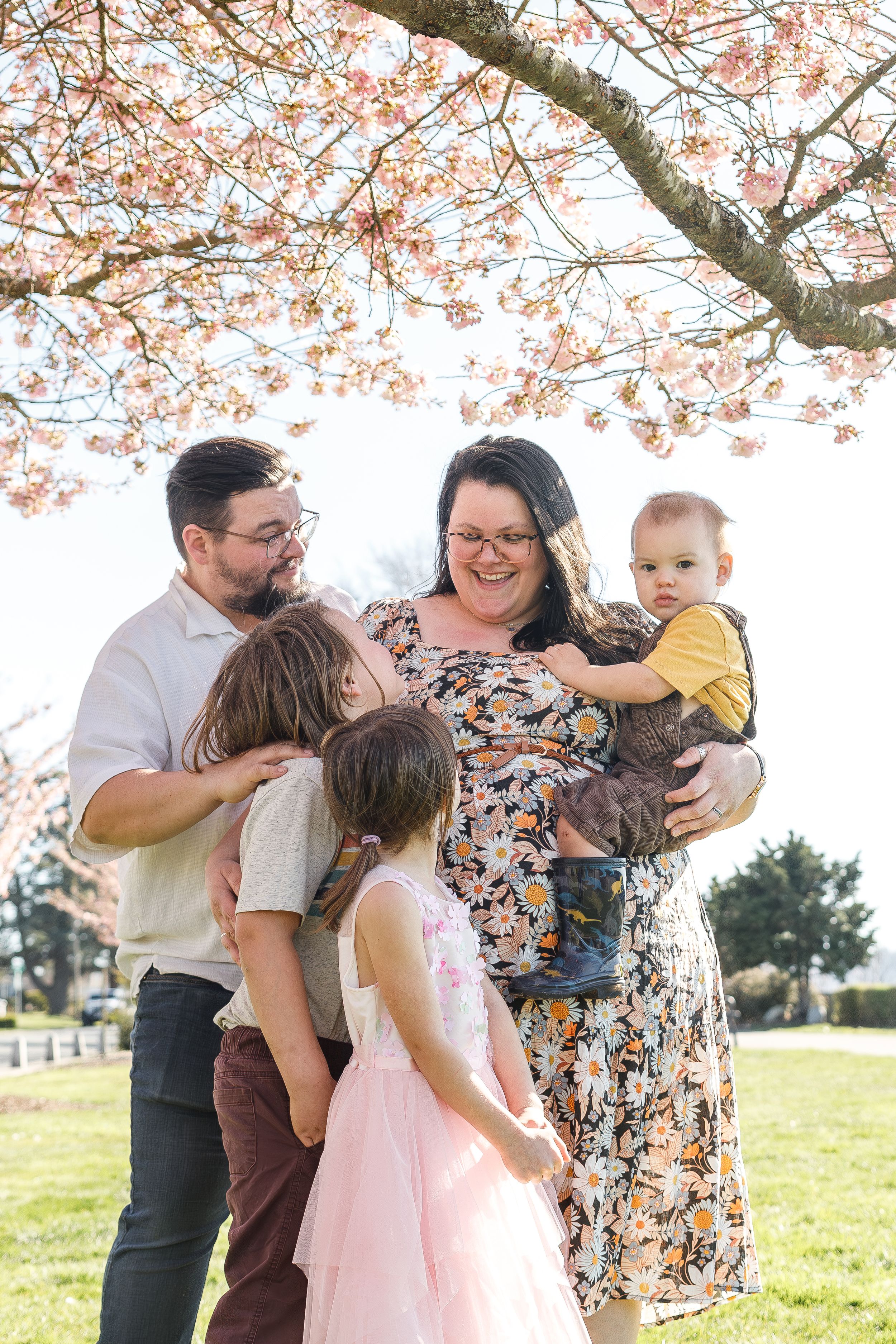 Spring family portrait under cherry blossoms in a park setting.