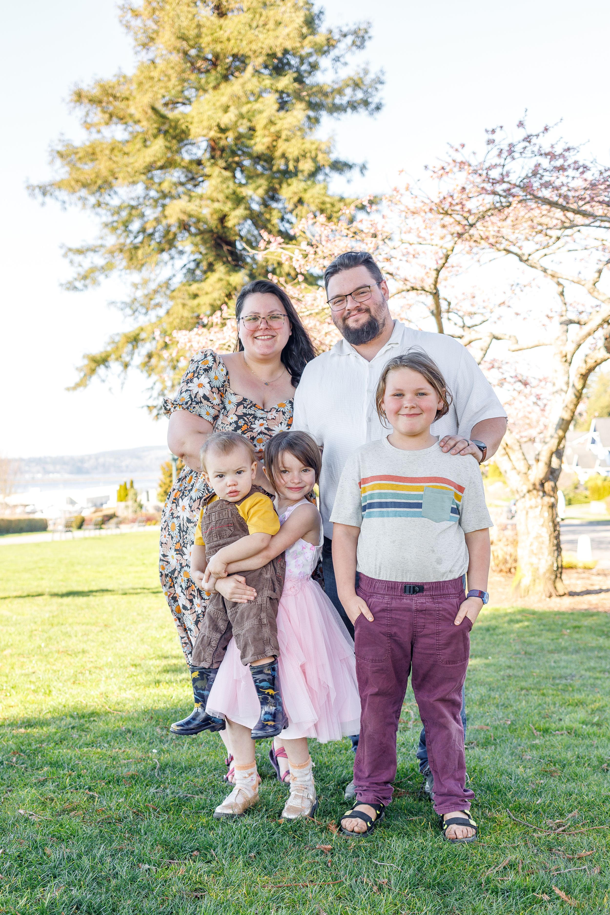 Family group portrait in a park with blooming trees and sunshine.