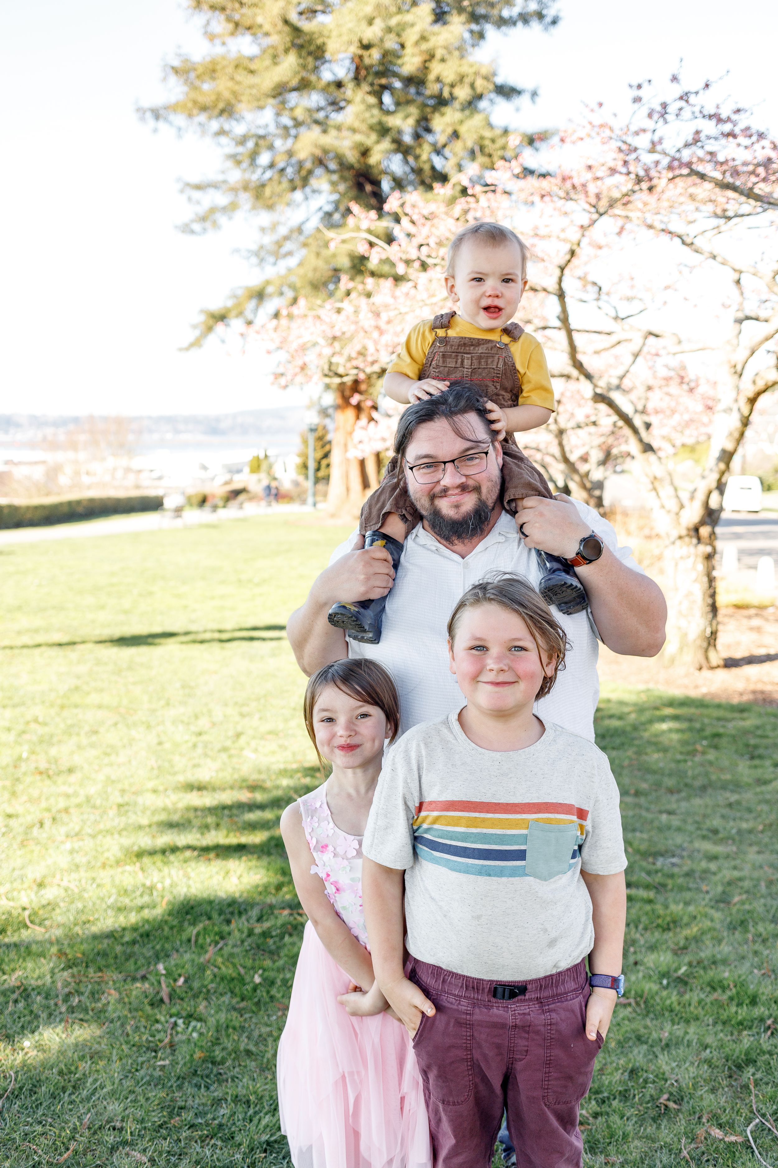 A family poses together outdoors on a sunny day with trees in the background.