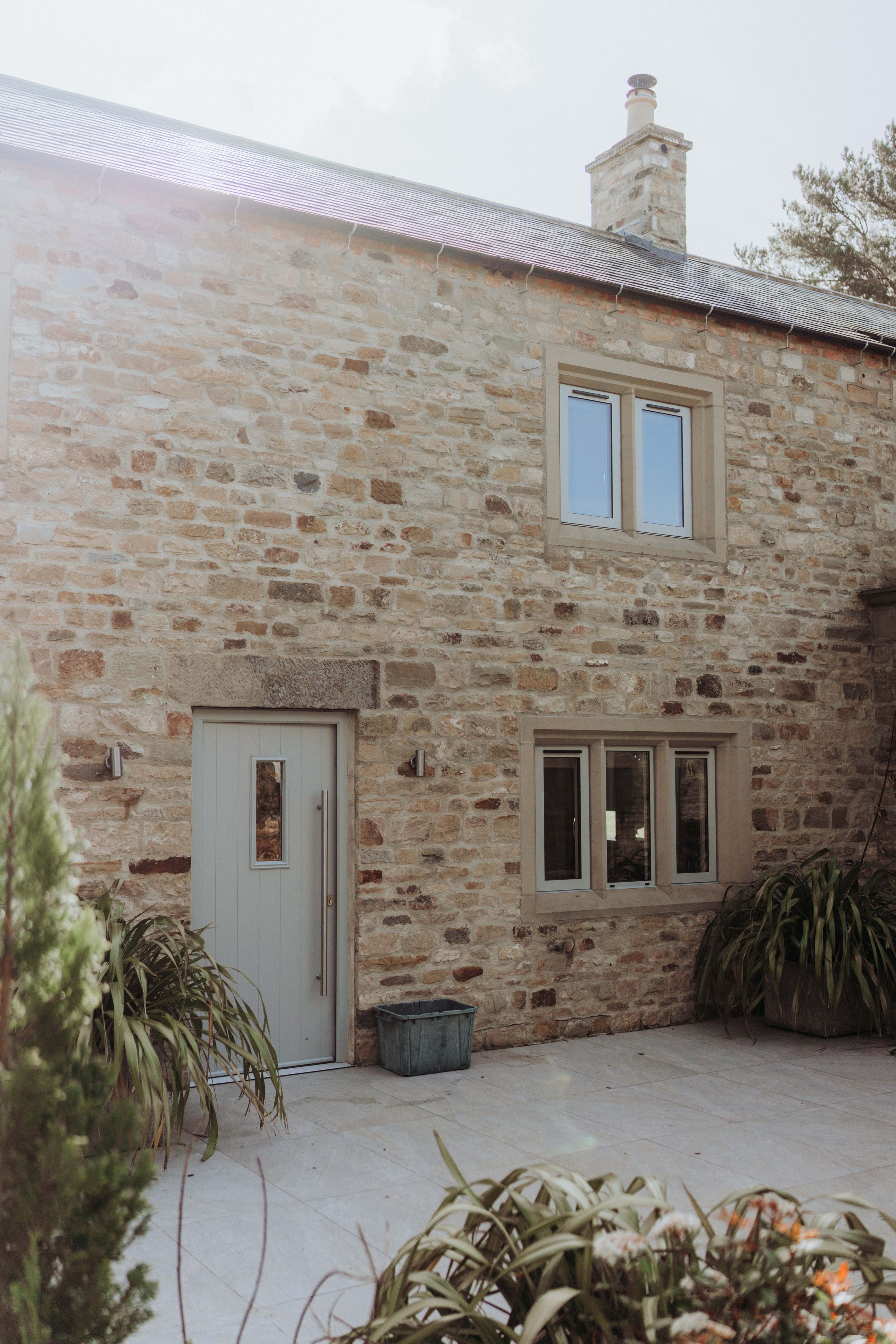 Stone cottage exterior with grey door and windows featuring traditional rustic architecture.
