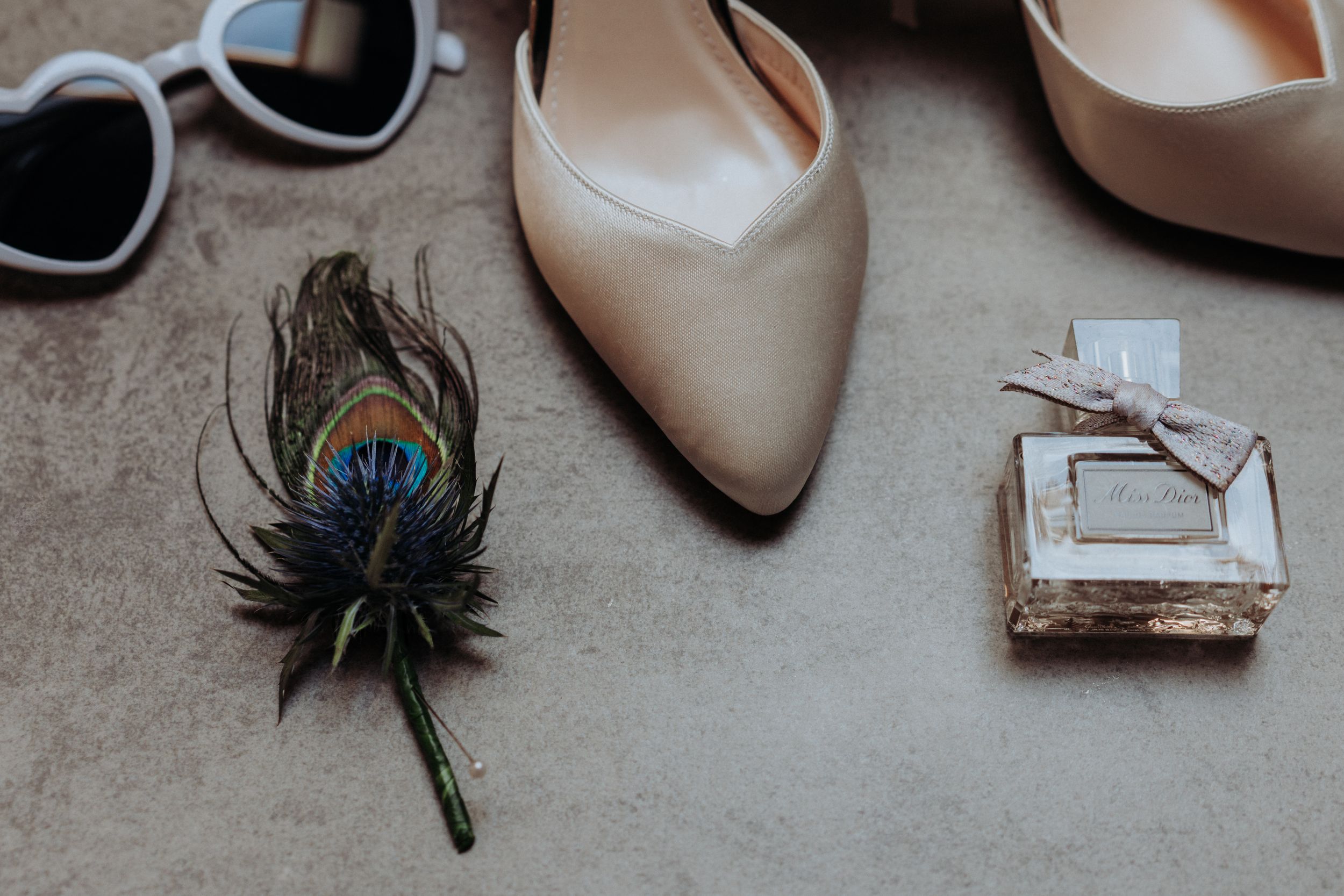 Wedding accessories including nude heels, sunglasses and peacock feather boutonniere.