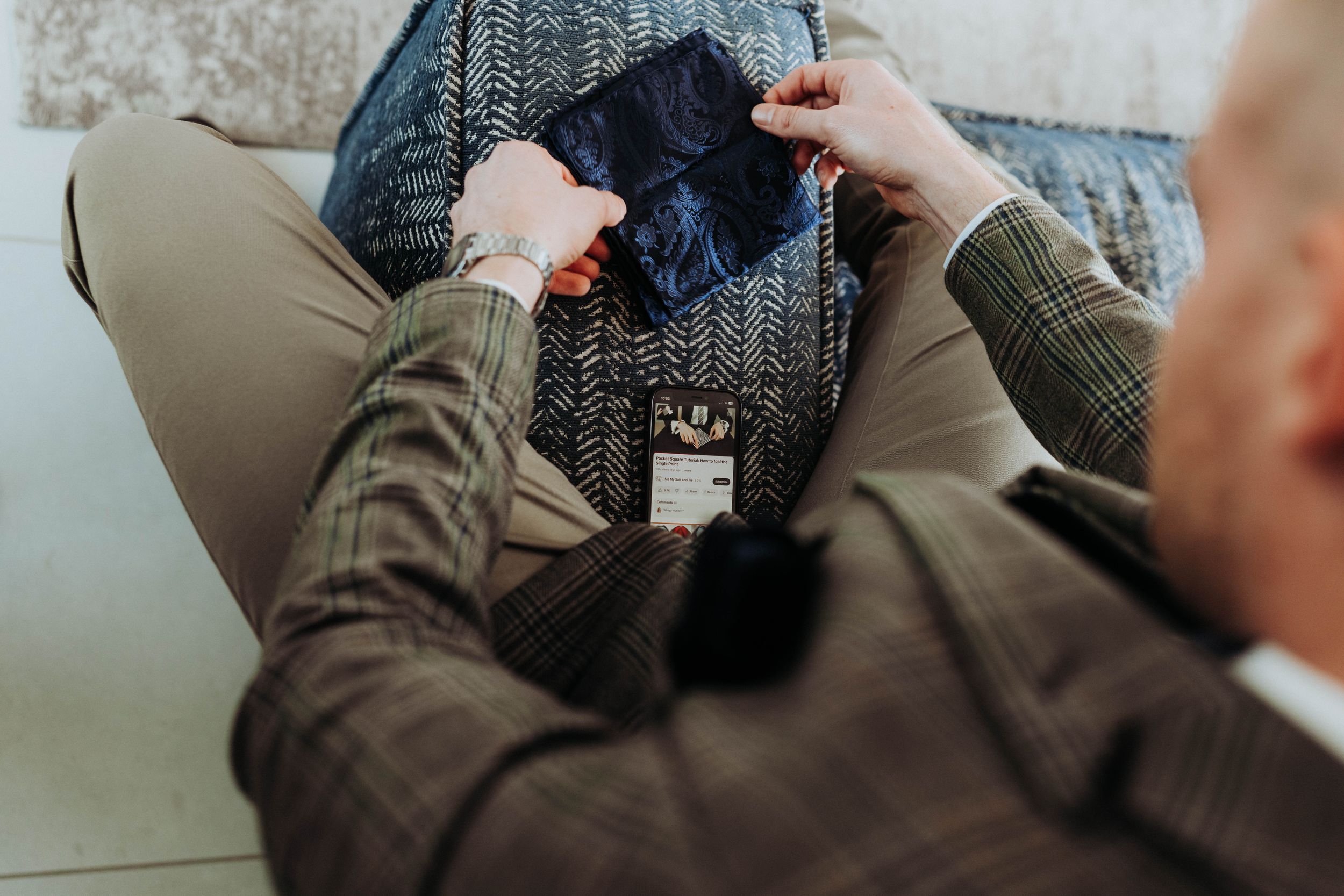 Close-up of hands adjusting and fixing details on a dark gray tweed suit jacket.