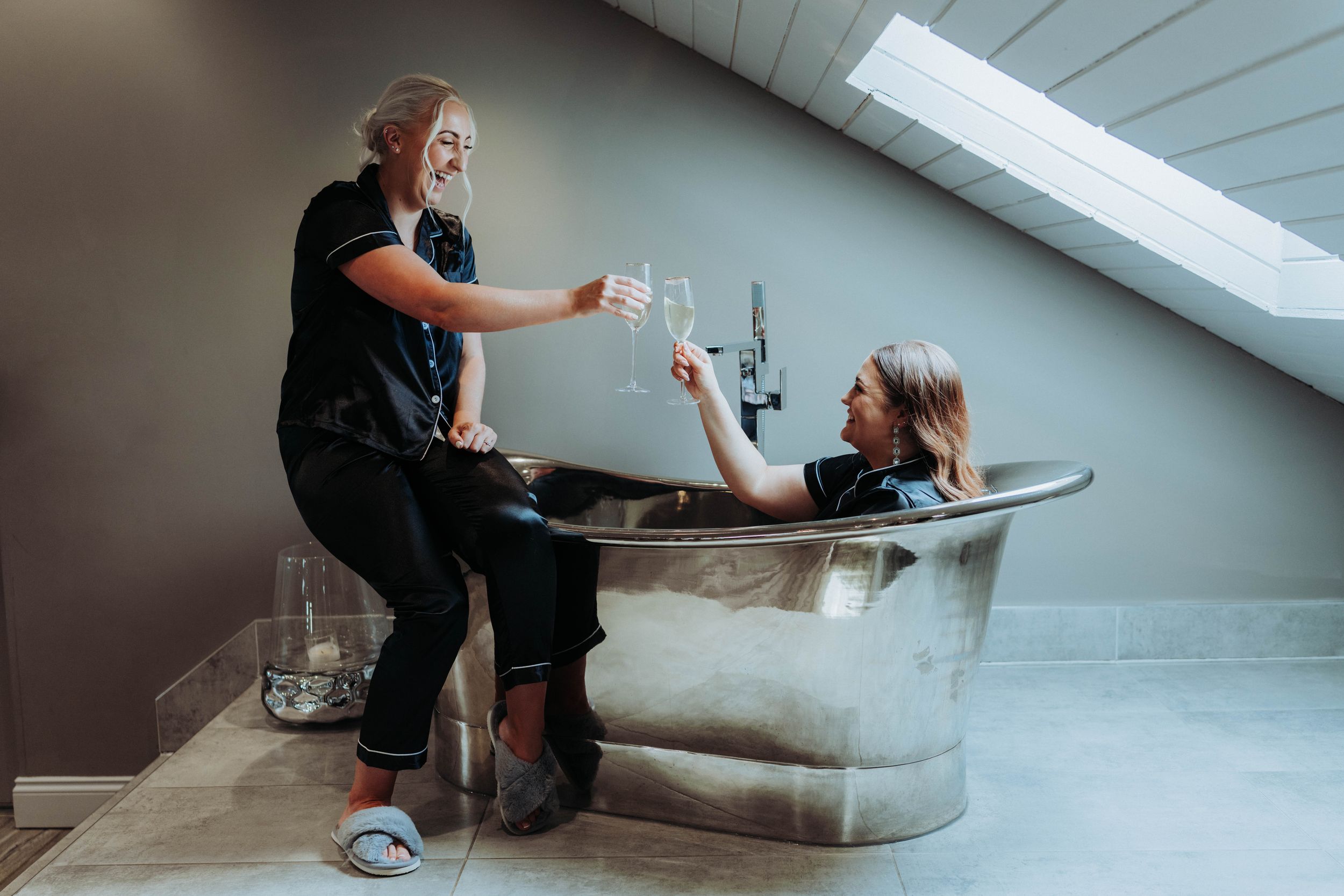 Two people sharing drinks and conversation beside vintage clawfoot bathtub.