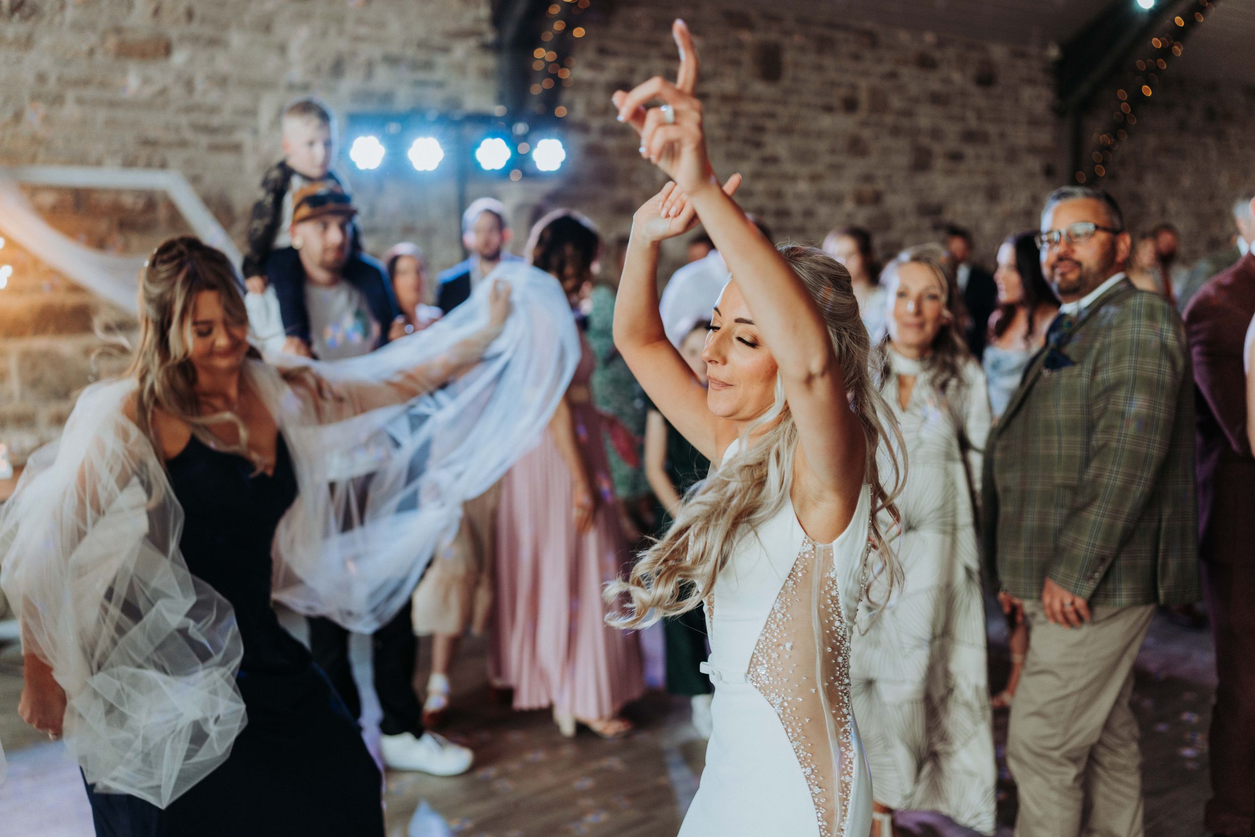 Wedding celebration with guests dancing energetically in rustic brick-walled venue.