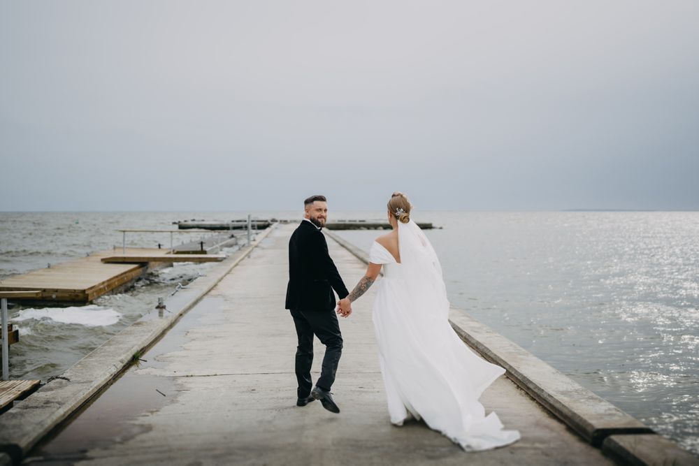 Wedding couple walking along wooden pier by the ocean.