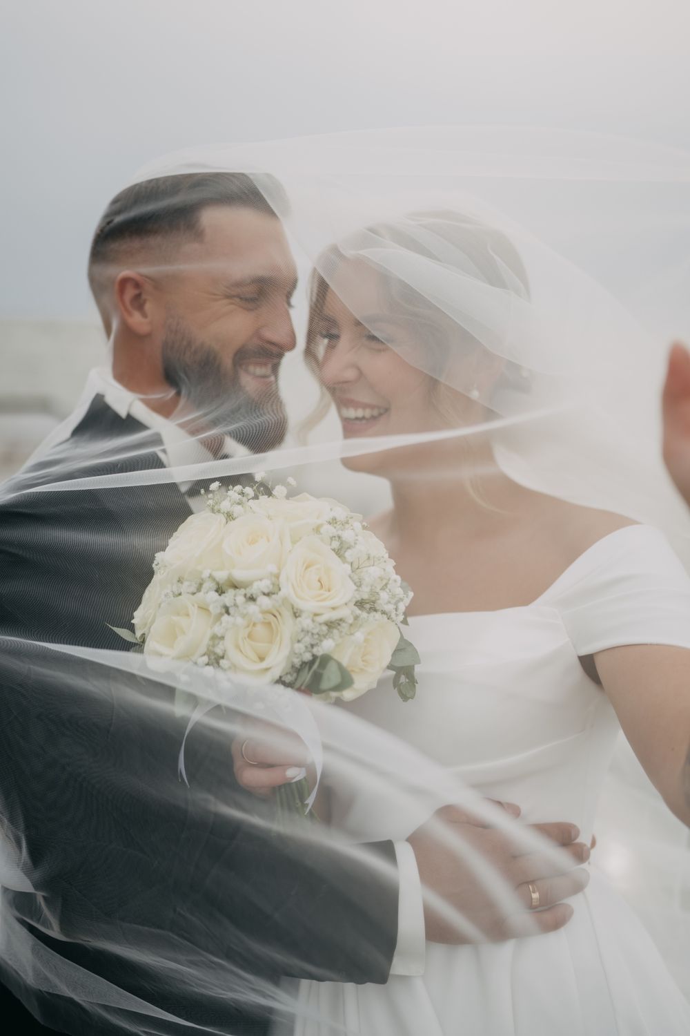 Candid wedding moments captured through a delicate veil with white floral bouquet.