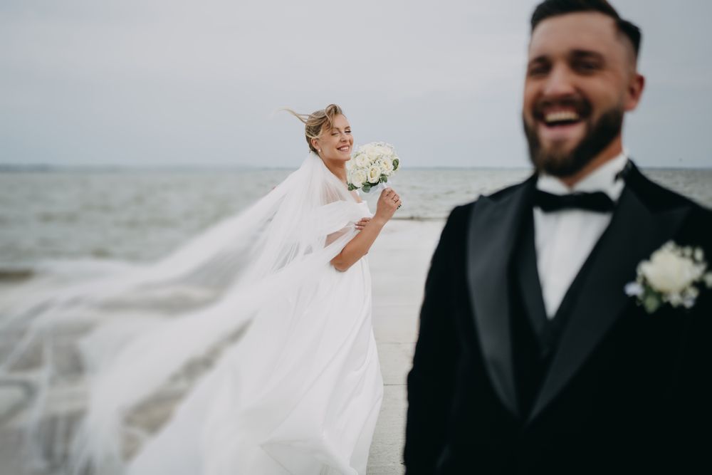 Joyful outdoor wedding photography session with flowing veil against coastal backdrop.