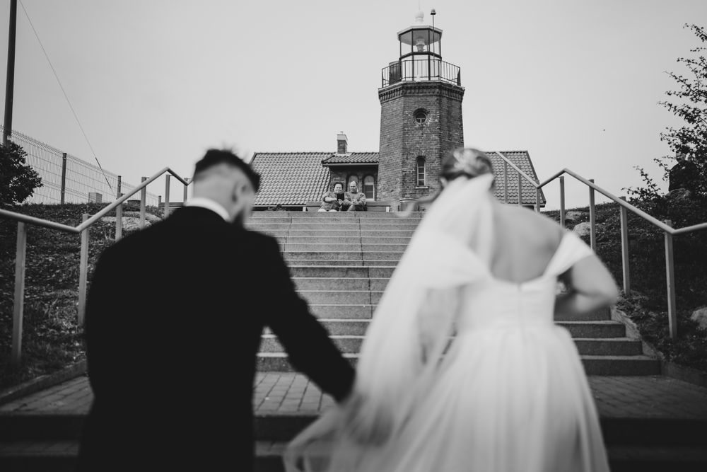 Wedding couple poses near a lighthouse with dramatic veil movement.