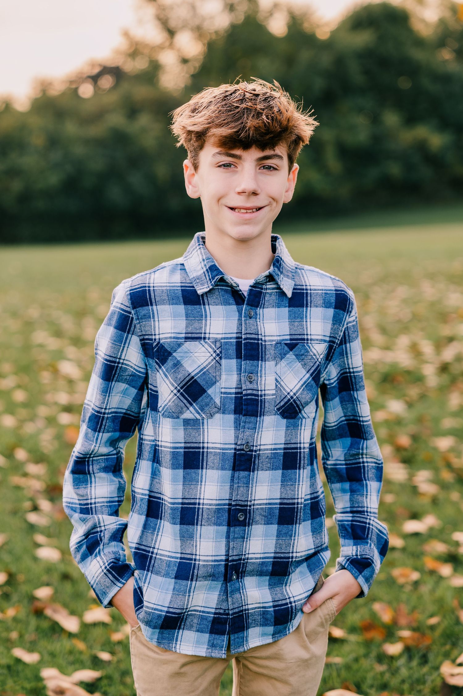 Teenager wearing blue plaid shirt smiles while posing in outdoor autumn setting in Metro Detroit.