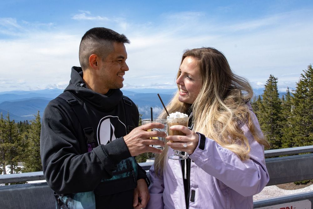 Couple toasting drinks on a snowy mountain overlook on a sunny day at Timberline Lodge.