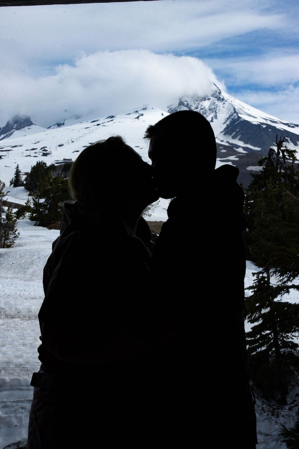 Silhouette of a couple kissing with a snow-capped Mount Hood and evergreen trees in the background.