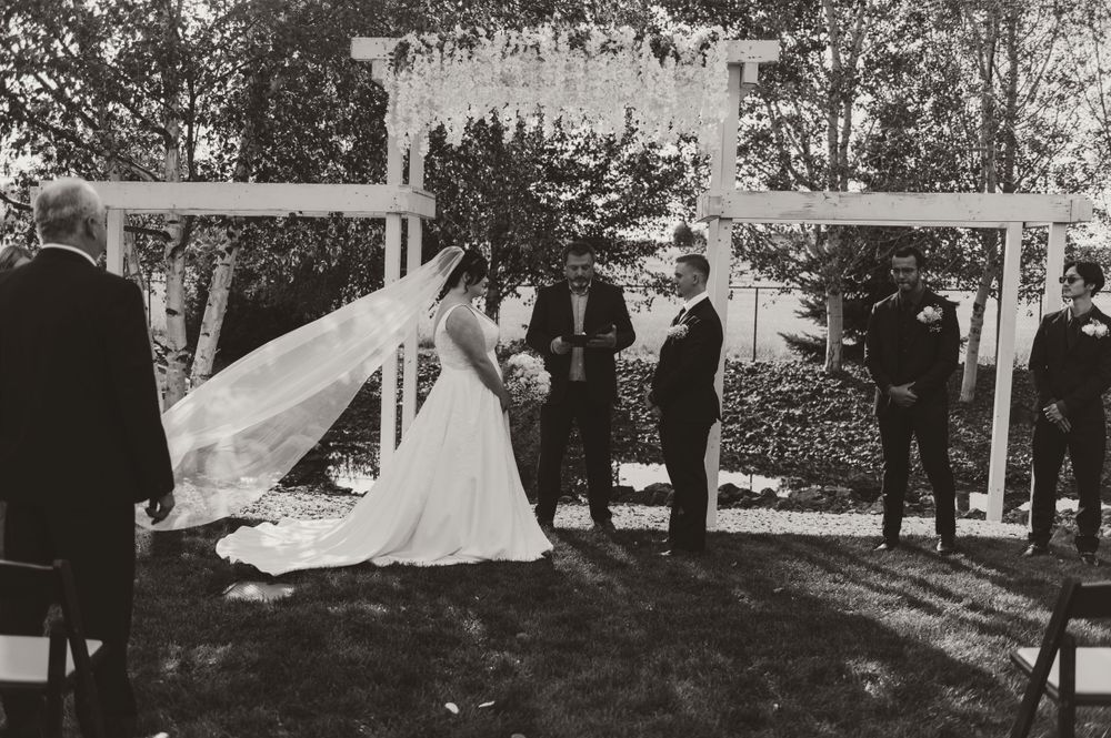Black and white photo of outdoor wedding ceremony under white tent with flowing veil.