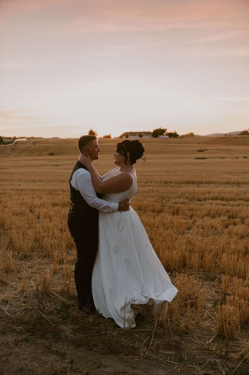 Couple embracing in a golden wheat field during sunset on their wedding day.