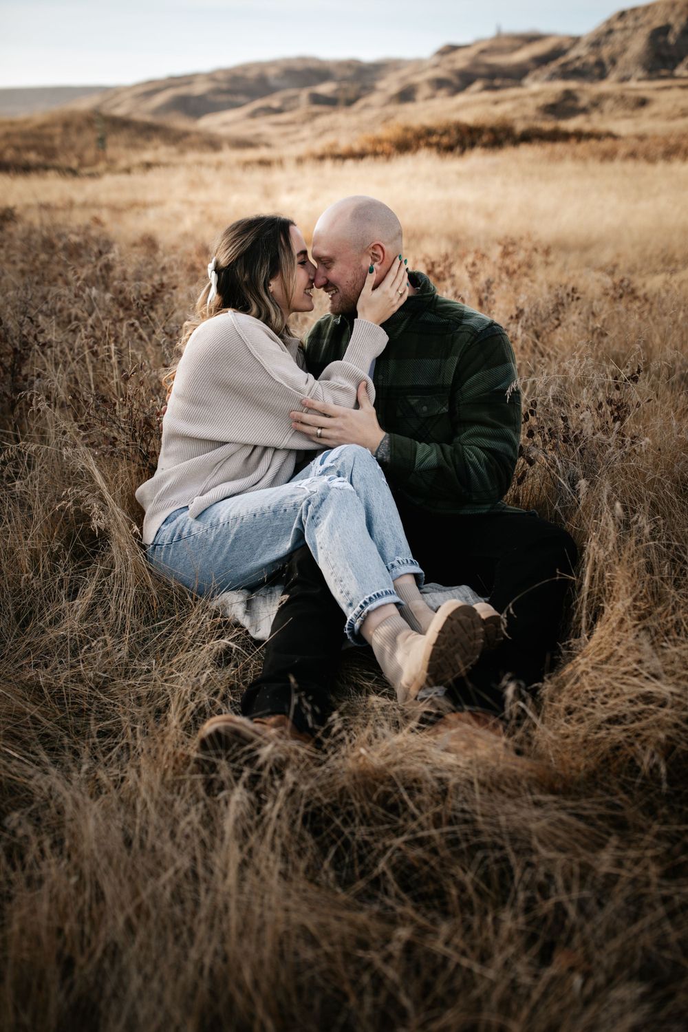 Two people share tender moments while sitting in dry grass during sunset.