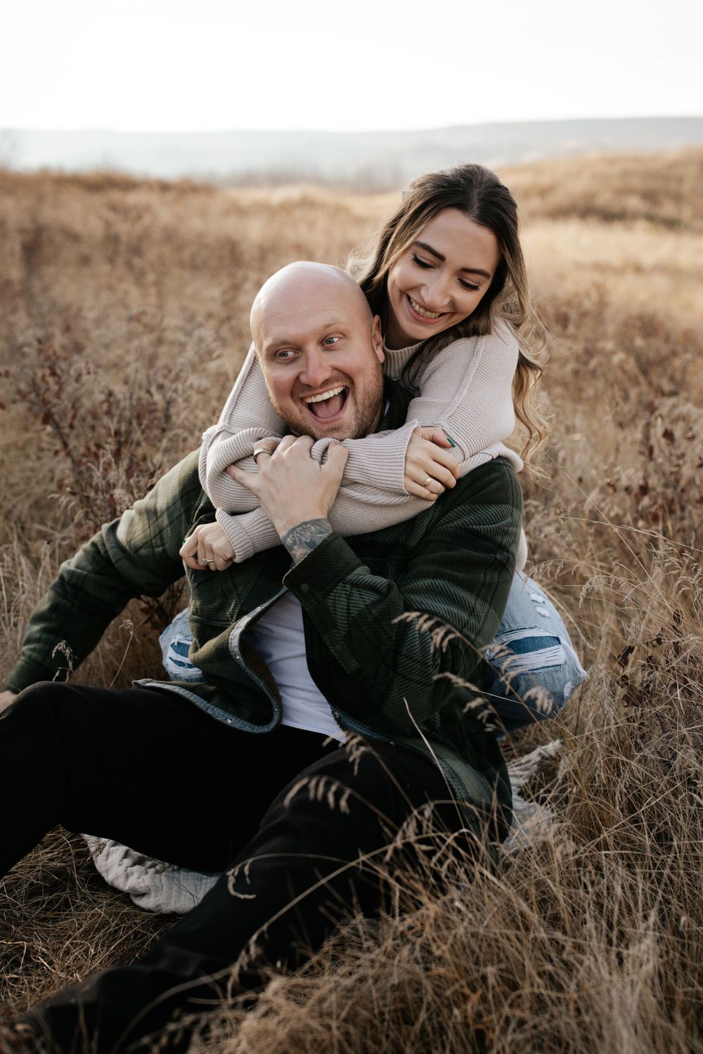 A playful couple laughs while embracing in a golden field.
