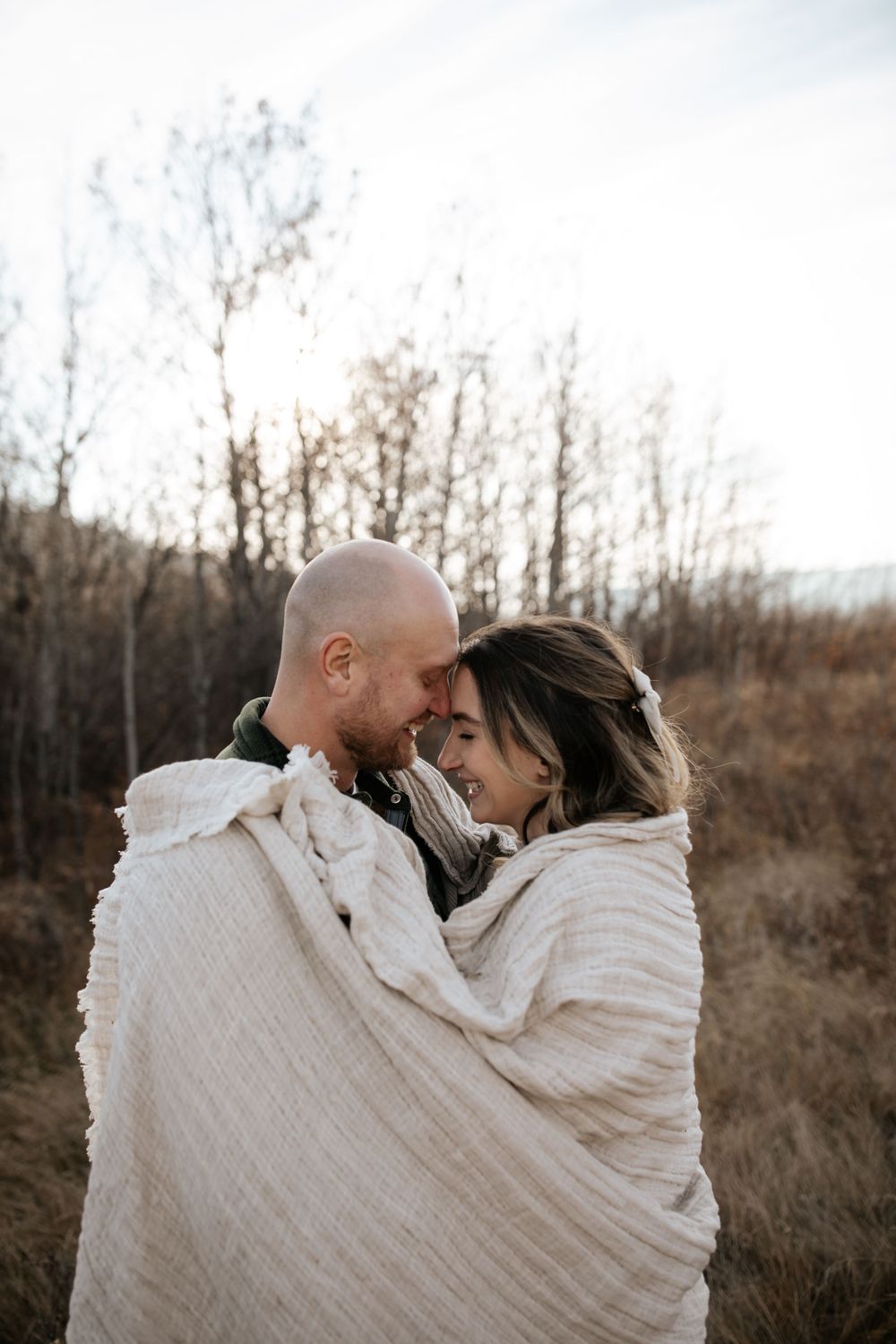 A couple wrapped in a white blanket shares an intimate moment outdoors.
