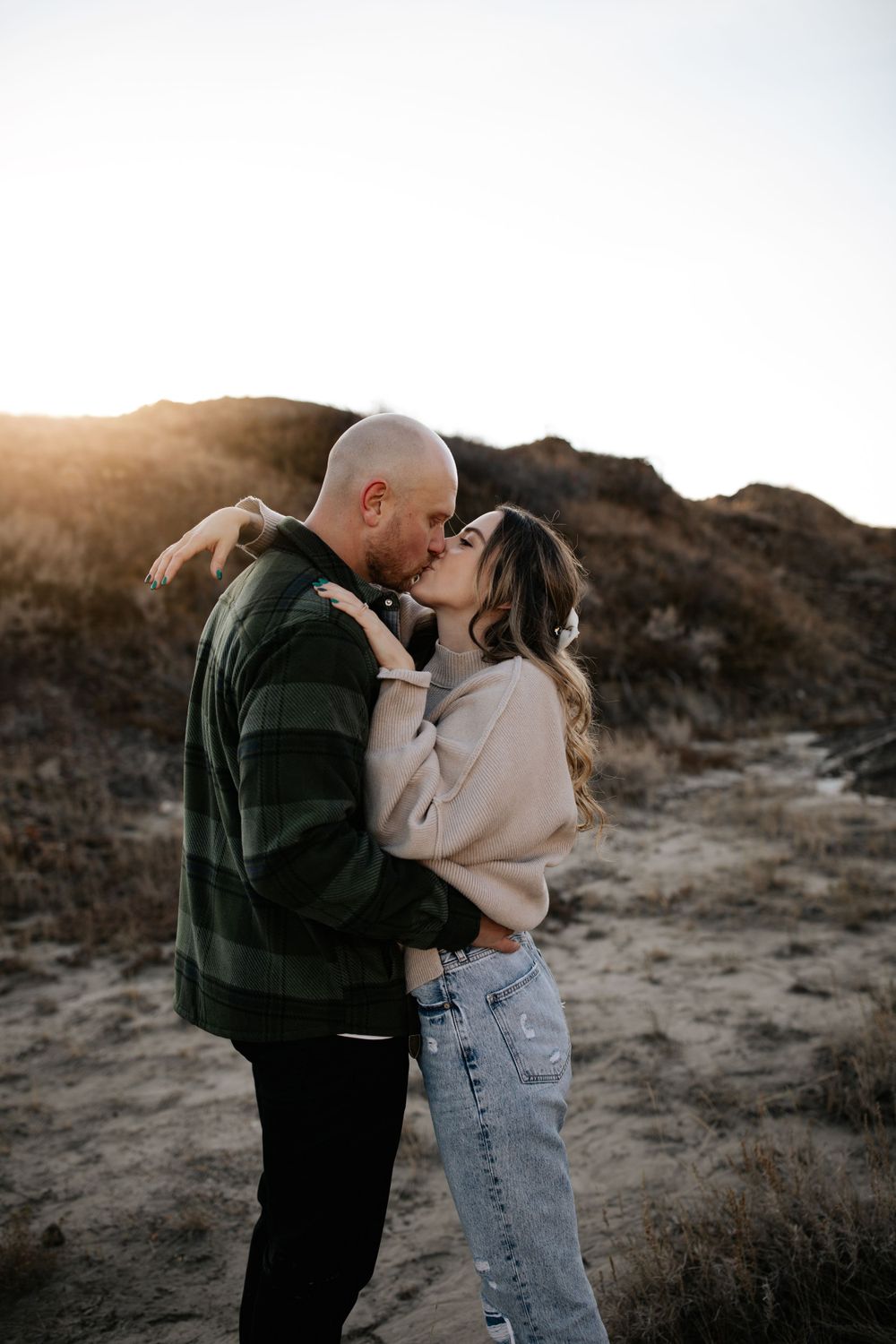 A tender moment between a couple on a hillside during sunset.